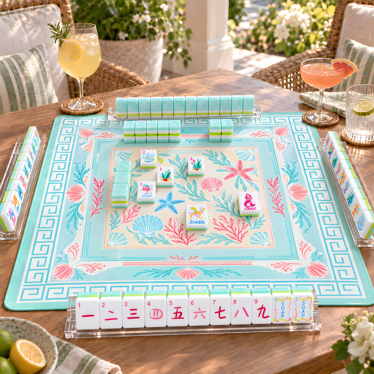 Mermaid American mahjong tiles set up for a game on an aqua seashell mat on a sunny terrace, with pearly aqua tile walls and racks
