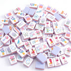 Violette American mahjong tiles scattered face up and face down, showing pale lavender backs and coral layered edges